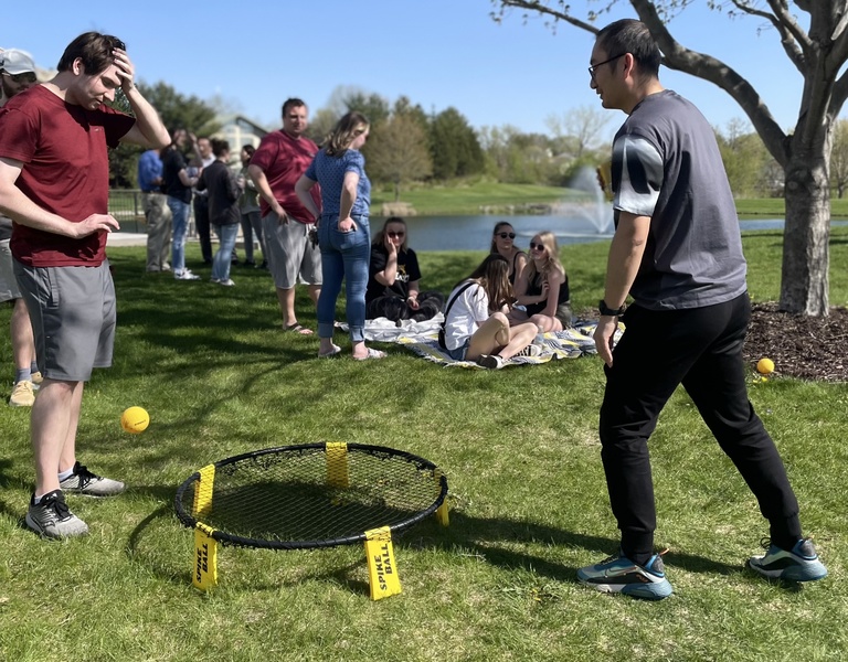 spike ball game with students sitting on grass in background